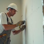 Artisan découpant du placo déjà posé avec des outils de sécurité.