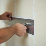 Un bricoleur découpe du placo déjà posé avec un cutter et une règle.