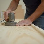 Artisan préparant du lambris pour application d'enduit, outils visibles.